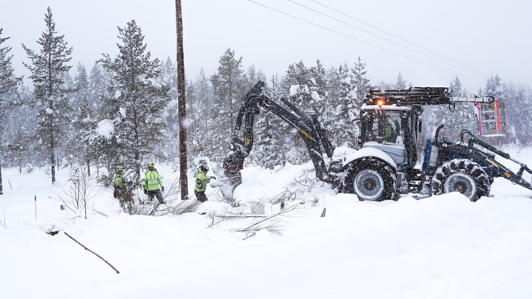 Arbete med underhåll av elnät och elledningar av elnätsbolaget BTEA i djup snö med hjälp av en traktorgrävare.