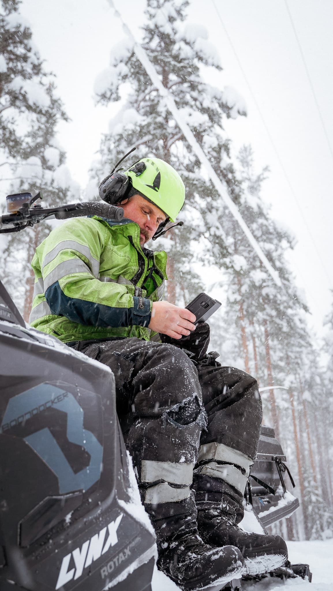 Personal från BTEA på en skoter i skogen, kontrollerar Ledningskollen på sin mobil för att säkerställa arbetet nära elledningar.