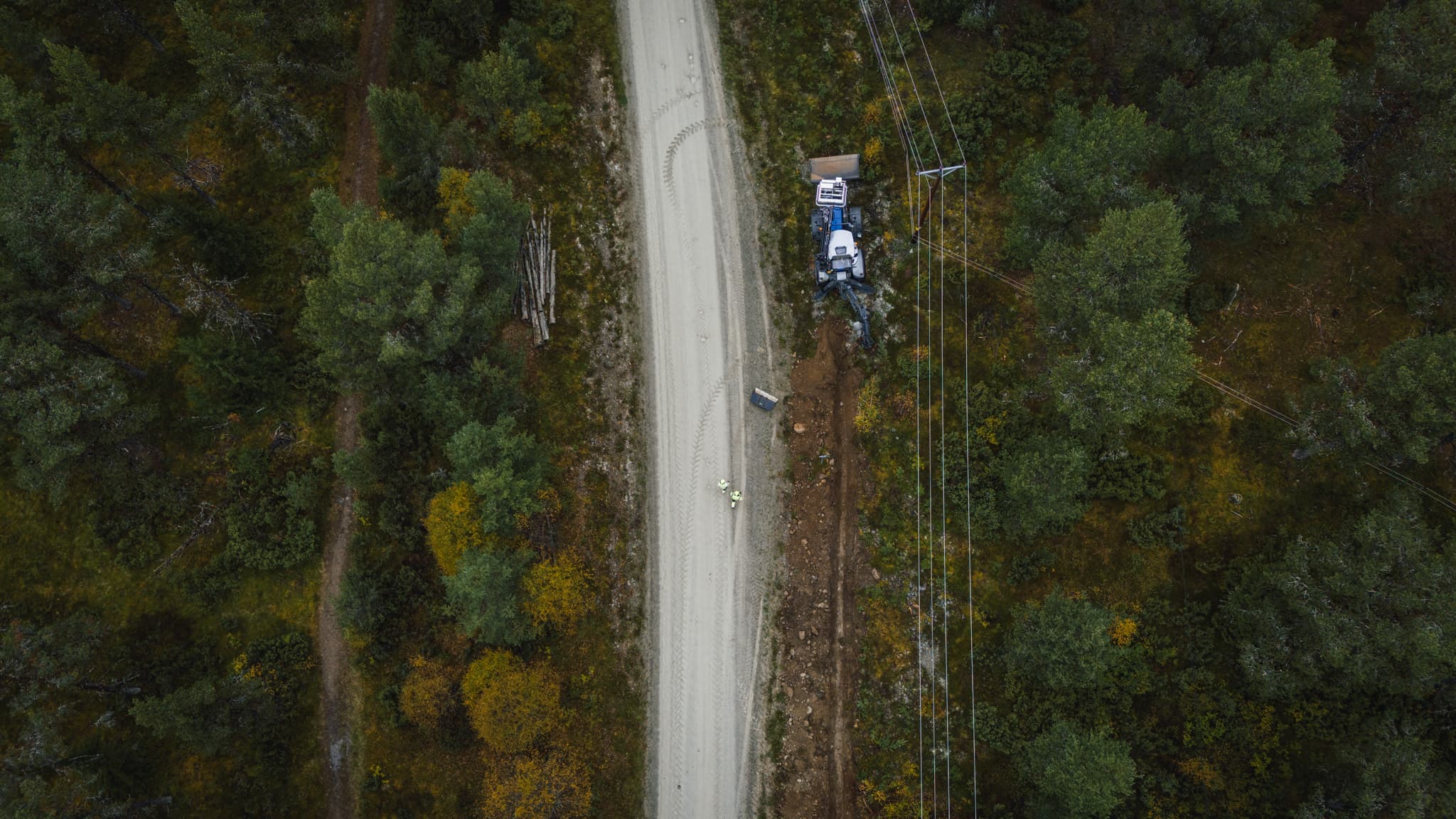 Grävarbete invid kraftledningar längs en väg fotat ovanifrån